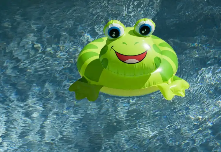 A green frog-shaped inflatable pool float is floating on the surface of clear blue water.